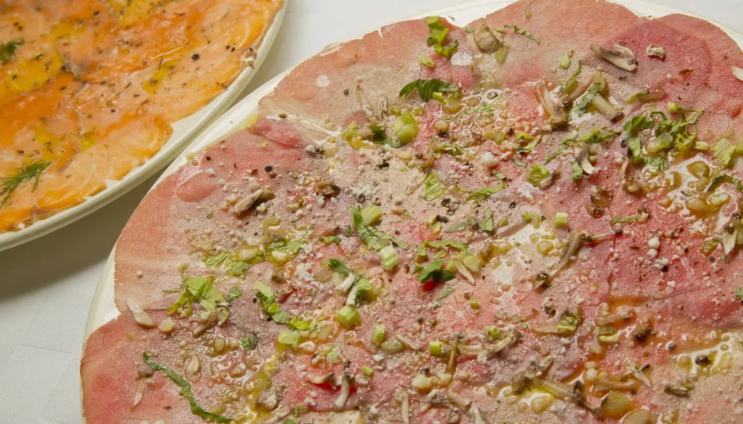 Prato de carpaccio de carne finamente fatiado com ervas frescas, queijo e azeite no restaurante Casa Nostra.