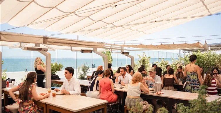 Clientes a desfrutar de uma refeição na esplanada movimentada do restaurante Casanova, protegida por toldos e voltada para a água.