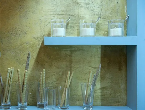 Prateleira azul com copos de grissini crocantes e frascos de condimentos em fundo rústico no restaurante Casa Nostra.