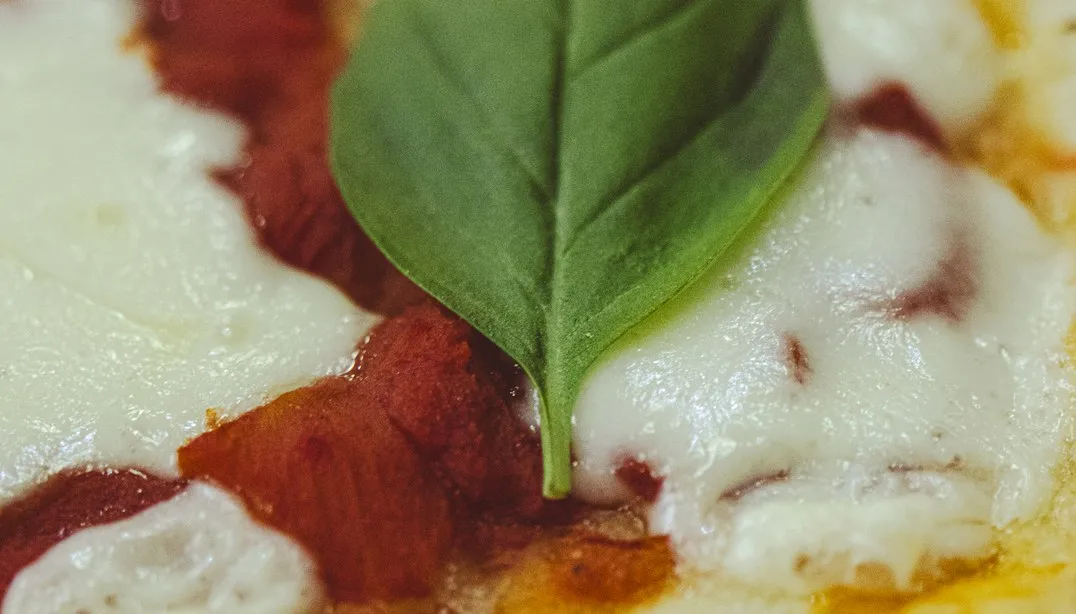 Close-up de pizza margherita artesanal com molho de tomate, queijo mozzarella derretido e folha fresca de manjericão da Pizza a Pezzi.
