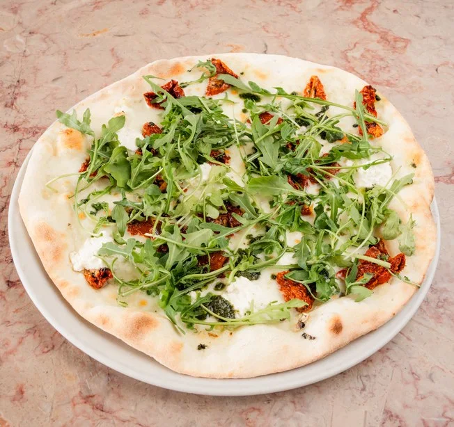 Close-up de pizza napolitana com queijo derretido, fatias de tomate seco e folhas frescas de manjericão no restaurante Casanova.
