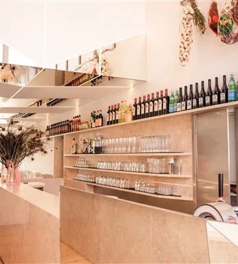Balcão em pedra clara com prateleiras de garrafas de vinho, copos alinhados e espelhos decorativos no restaurante Casanova.