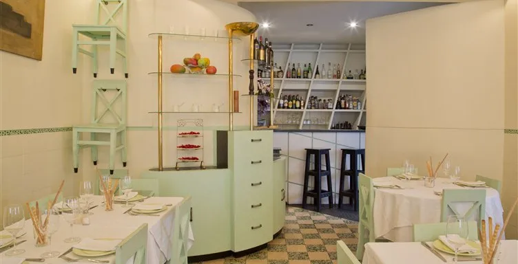 Perspetiva do salão do restaurante Casa Nostra mostrando mesas redondas e retangulares, móvel verde de apoio e acesso ao balcão de bar ao fundo.