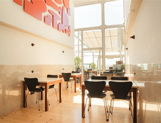 Salão interior iluminado do restaurante Casanova com mesas de madeira, cadeiras pretas e arte moderna em relevo na parede.