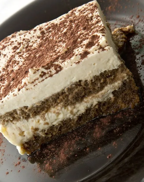 Porção de tiramisù cremoso com camadas de café e cobertura de cacau em pó servida em prato escuro no restaurante Casa Nostra.